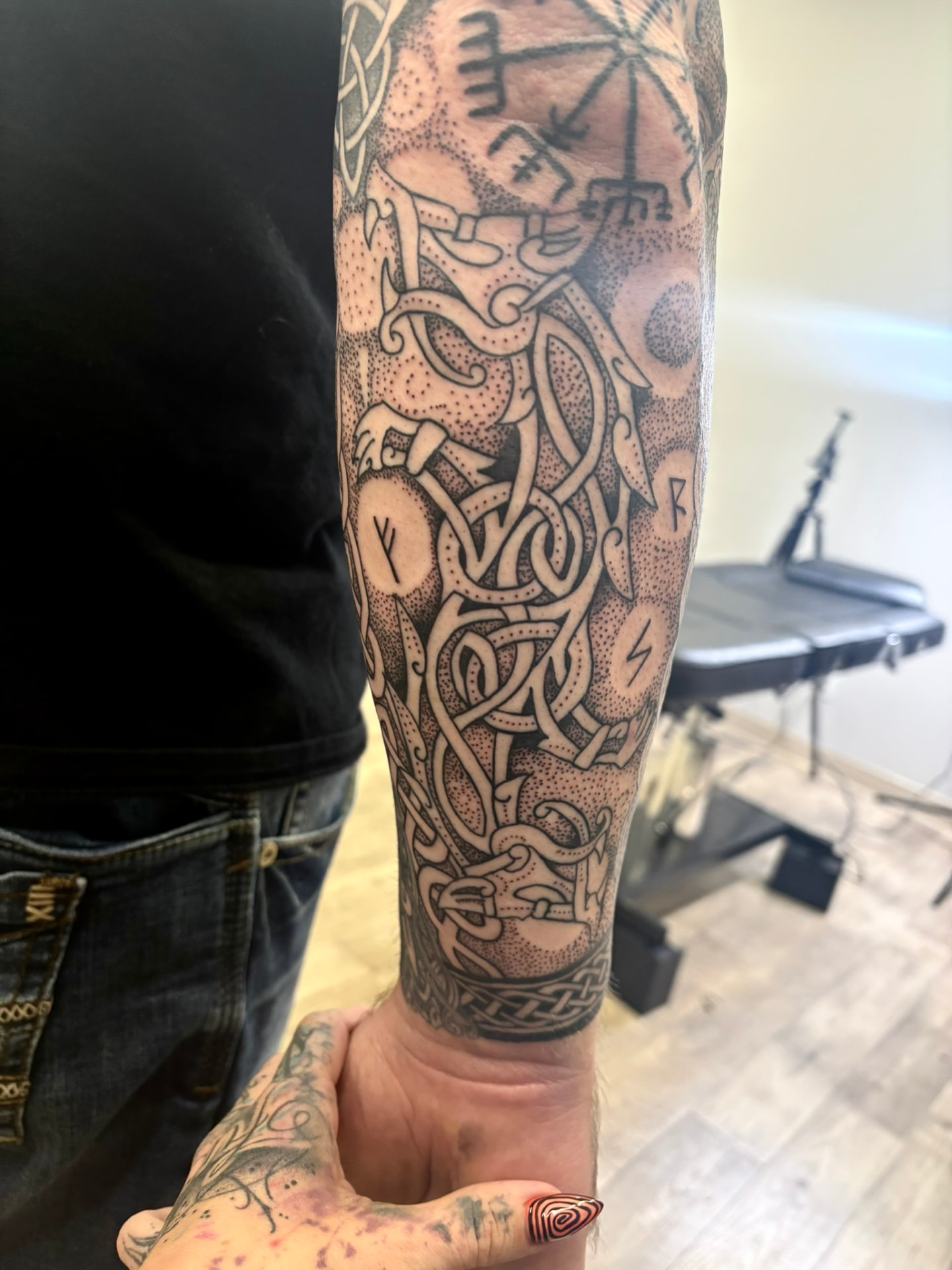 Blackwork forearm tattoo of intertwined Norse serpent beasts, runes, and dense dotwork shading