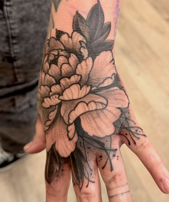 Black and grey peony tattoo covering the back of a hand