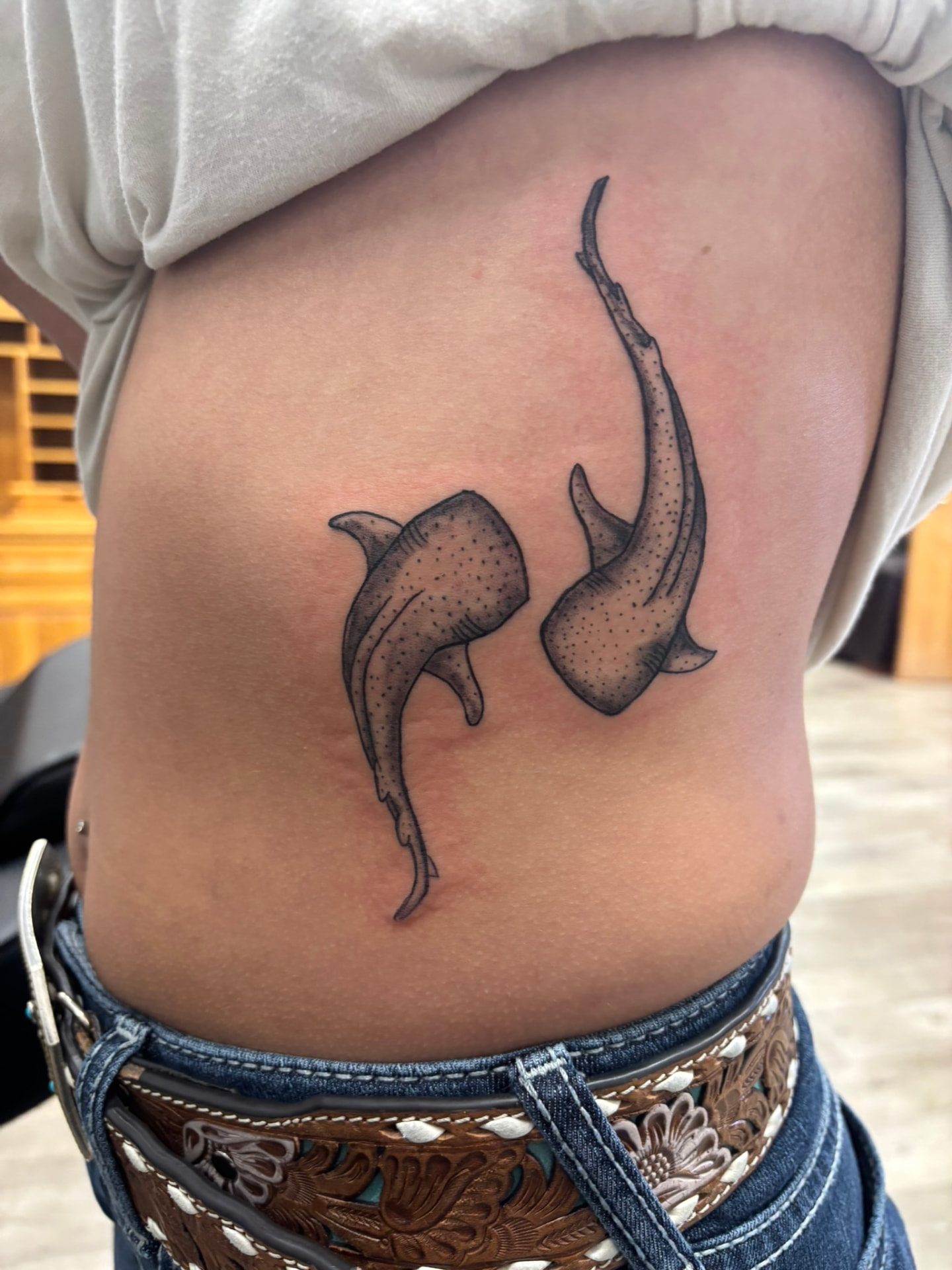Black and grey tattoo of two whale sharks swimming downward along the ribs with stippled dot shading