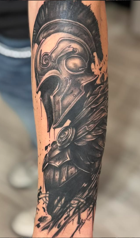 Black and grey forearm tattoo of a Spartan warrior helmet with a rose and trash-polka brush strokes
