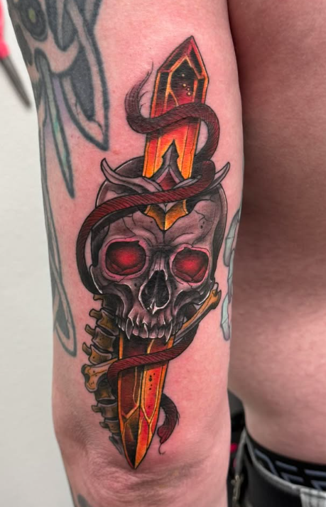 Color neo-traditional forearm tattoo of a skull with red eyes pierced by a golden dagger wrapped in a serpent