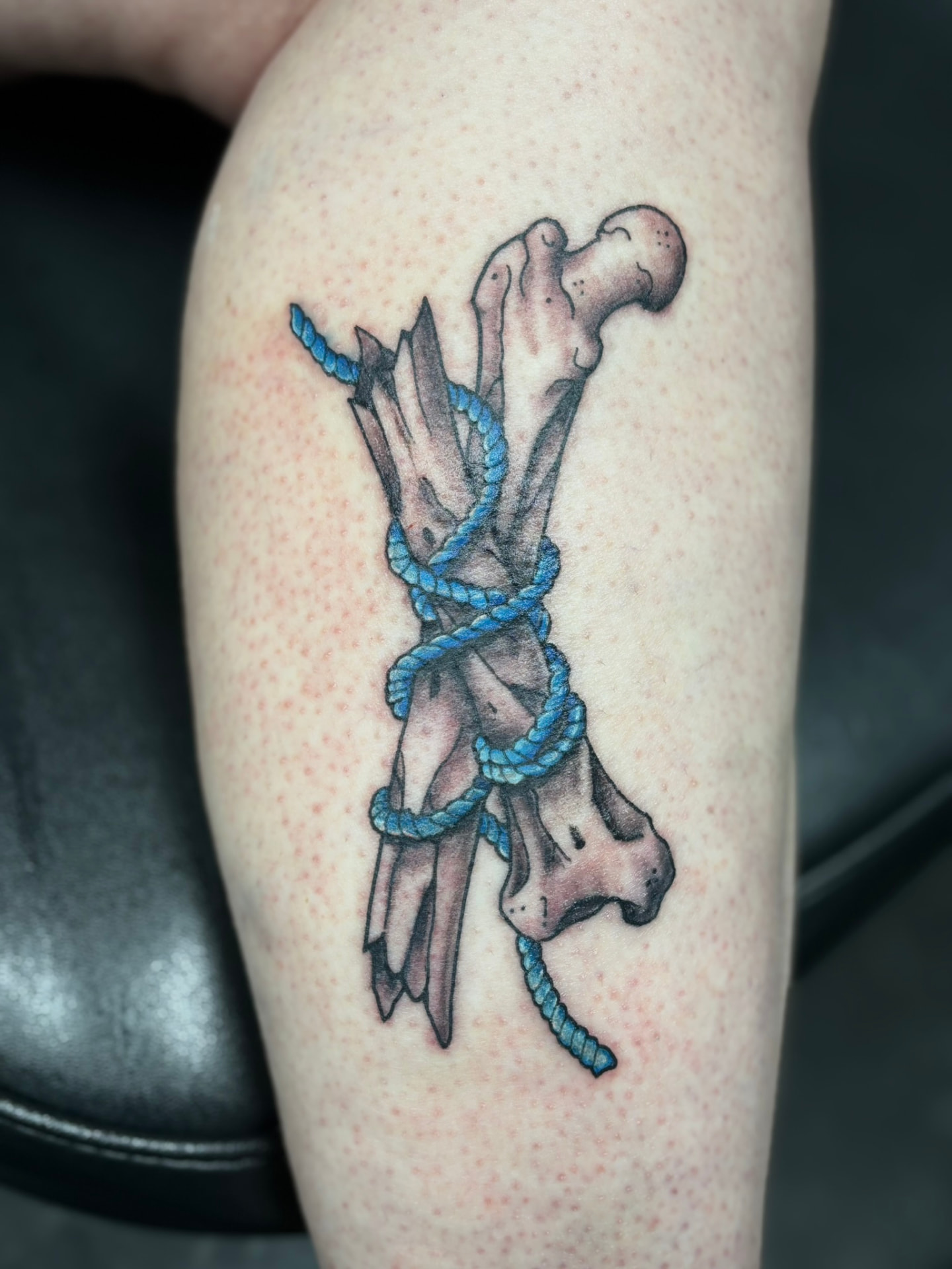 Color tattoo of broken bone fragments bound together with a bright blue braided rope