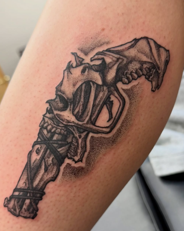 Dotwork tattoo of a revolver built from an animal skull and bound bone